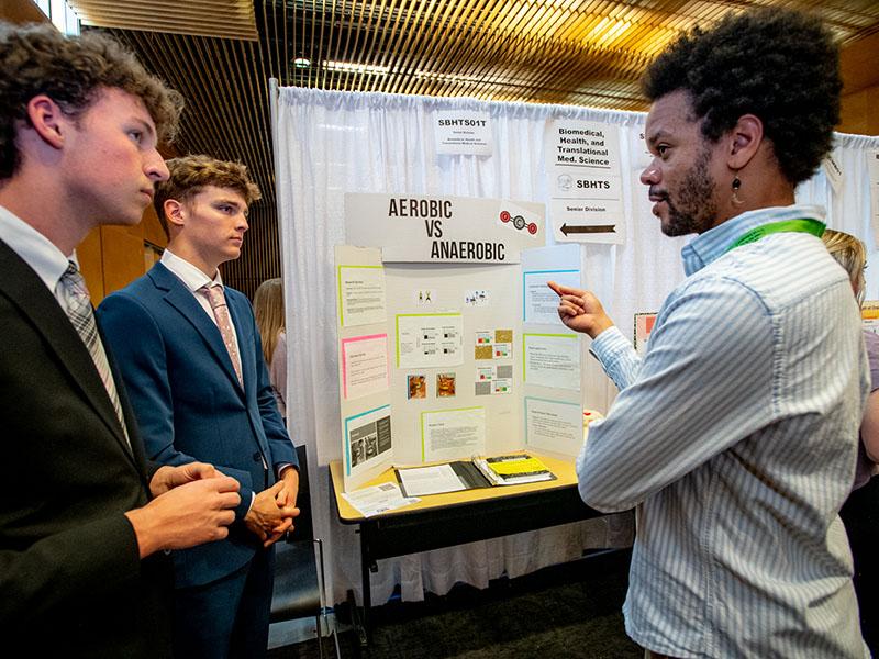 Holy Cross juniors Kameron Callahan and Aaron Guichard, left to right, listen as GNOSEF judge Adam Julien comments on their research about aerobic exercise as compared to anaerobic exercise.