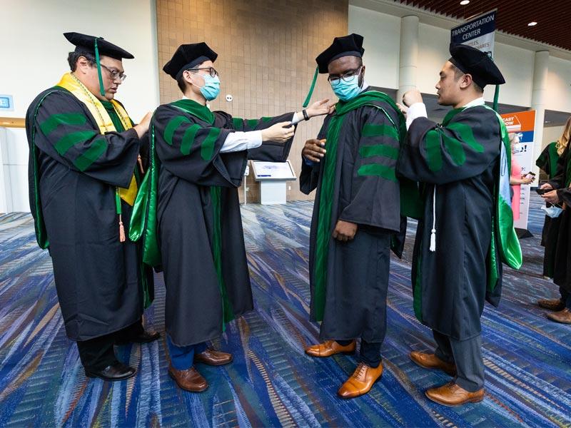 Candidates for Doctor of Medicine help each other with their regalia before the start of the 2021 School of Medicine Commencement ceremony. Candidates for Doctor of Medicine help each other with their regalia before the start of the 2021 School of Medicine Commencement ceremony.