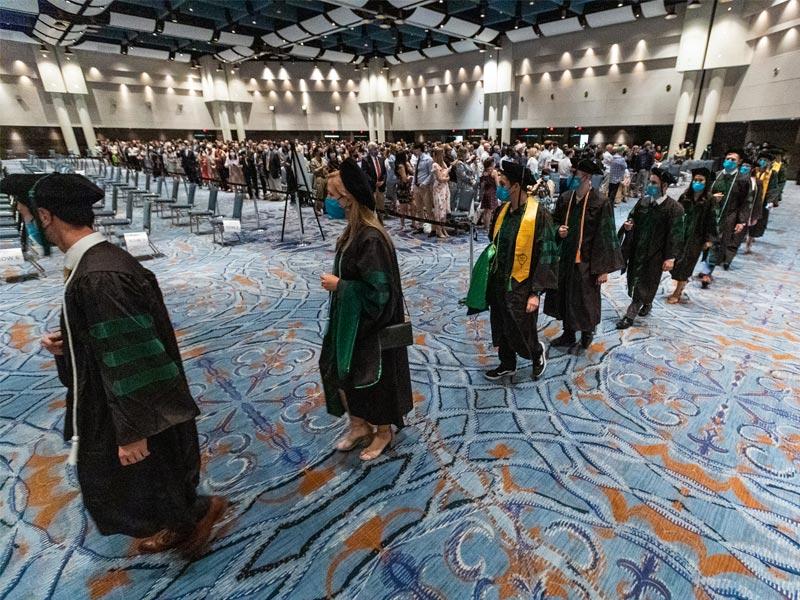 Holding their hoods, graduates walk past family and friends towards their seats. 