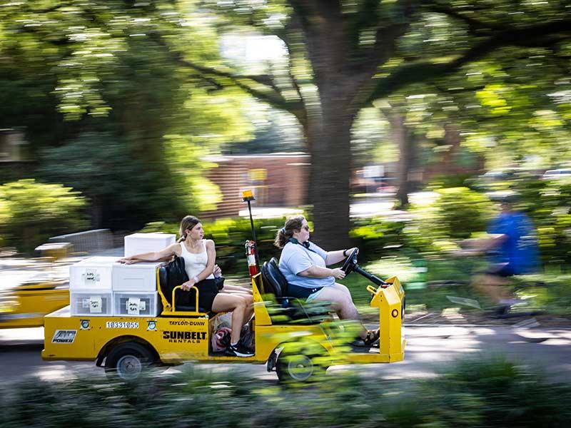 Move-in volunteers and Housing and Residence Life staff assist a student with their belonging by driving them to their residence hall. 