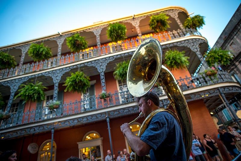 A sousaphonist performs an early evening serenade as sunlight rises on the third floor balcony at the corner of St. Peter and Royal Streets in the French Quarter