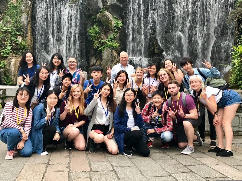 A group of students posing outdoors by a tree in Thailand