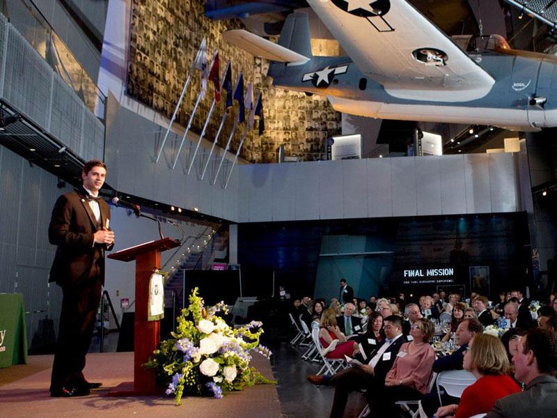 Man speaks at podium at awards gala in D-Day Museum
