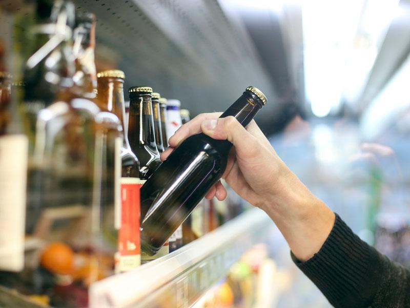 Hand reaching for beer bottle on store shelf