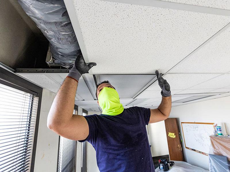 A repair man adds a new ceiling tile to damaged room
