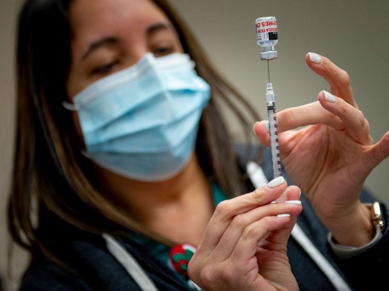 A nurse wearing face mask prepares to administer vaccine shot