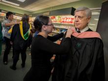 Dr. Hugh Robertson stands ready to be photographed as Lauren LaCaze adjusts his academic regalia during Grad Fest Downtown.