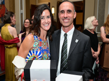 Smiling man and woman in formal wear hold black presentation boxes.