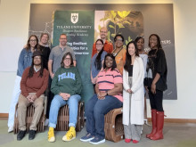 Eleven people smiling, posing in front of a Tulane University banner.