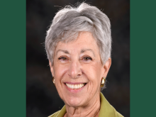 Smiling older woman with short gray hair, wearing a green top and gold earrings.