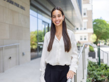 Smiling young woman in white blouse stands outside modern building.