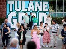 A student poses with their parents in front of a 'Tulane Grad' sign outside of Yulman Stadium. 
