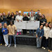Smiling group of students and adults holding two oversized checks on a stage.