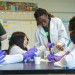 Students in lab coats and gloves doing a science activity with an instructor