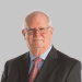 Older man in suit, tie, and glasses, smiling in a professional photograph.