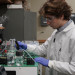 Young scientist in lab coat, glasses, and gloves, handling tubes on lab equipment.
