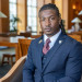 Man with dreadlocks in a suit and tie, looking at the camera, in a library.