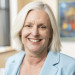 Smiling woman with white hair and a light blue jacket.