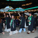 Joyful graduates in caps and gowns celebrating at night, holding umbrellas aloft in a stadium.