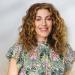 Smiling woman with long curly brown hair and a colorful floral top.
